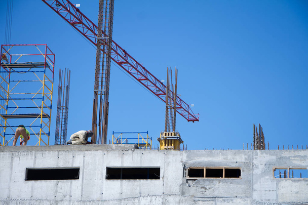 Unerkennbare Bauarbeiter an der Wand eines Neubaus vor dem Hintergrund von Betonkonstruktionen und blauem Himmel - Foto, Bild