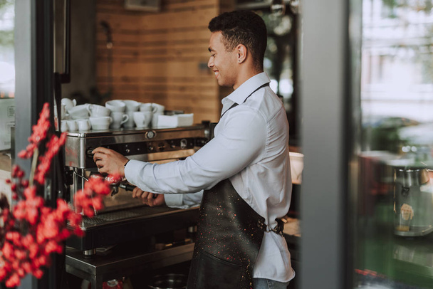 Handsome barman in black apron using professional coffee machine - Фото, зображення