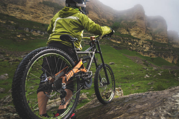 Rear view wide angle of a man on a mountain bike stands on a rocky terrain and looks at a rock. The concept of a mountain bike and mtb downhill - 写真・画像