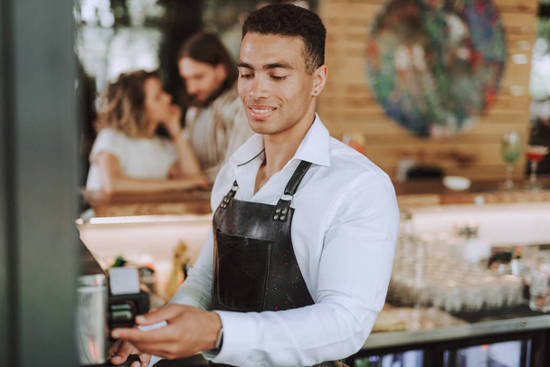 Handsome bartender in black apron making fresh coffee - Zdjęcie, obraz
