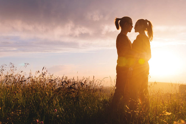 Σιλουέτ πορτραίτο ενός ρομαντικού νεαρού χίπστερ ζευγαριού στο προφίλ. Στέκεται σε μια αγκαλιά στη φύση στο ψηλό γρασίδι η έννοια της νεαρής οικογένειας και ένα ευτυχισμένο μέλλον μαζί - Φωτογραφία, εικόνα