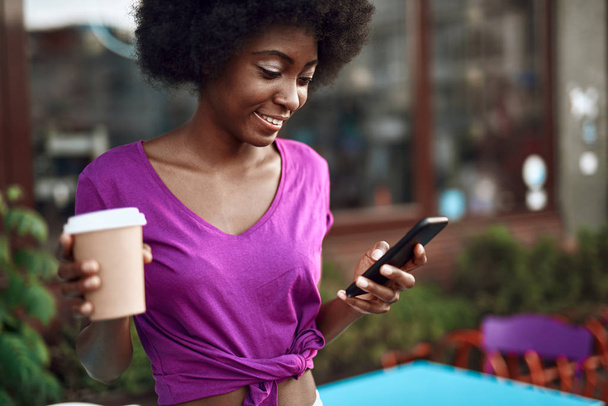 Cheerful afro-american girl typing on mobile phone outdoors - Foto, imagen