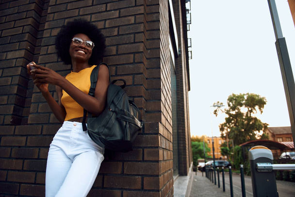 Joyful afro-american woman with bag holding smartphone outdoors - Фото, зображення