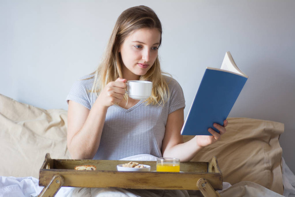 Woman reading a book and having breakfast. - Zdjęcie, obraz