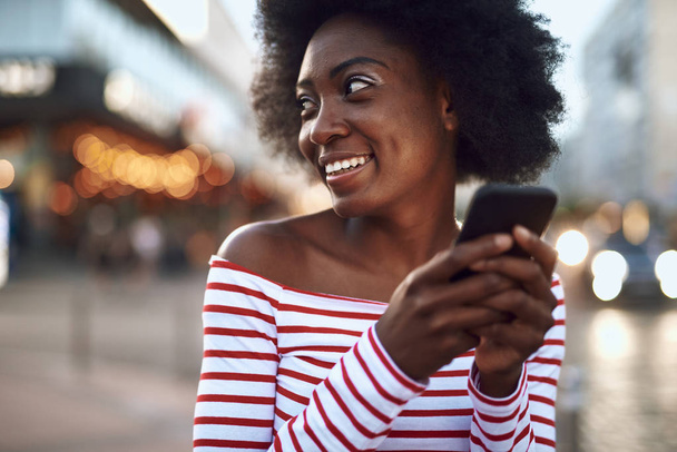 Joyful young lady is using smartphone outdoors - Фото, изображение