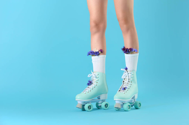 Legs of woman in vintage roller skates and with flowers on color background - 写真・画像
