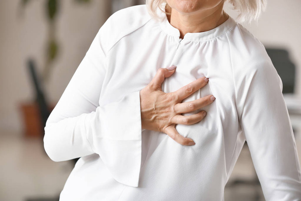 Mulher madura que sofre de ataque cardíaco no escritório, close-up
 - Foto, Imagem
