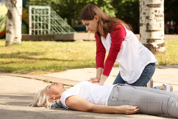 Female passer-by doing CPR on unconscious mature woman outdoors - Photo, Image