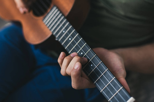 ukelele spel. een man die een kleine gitaar speelt. de performer schrijft de muziek op de ukulele thuis - Foto, afbeelding