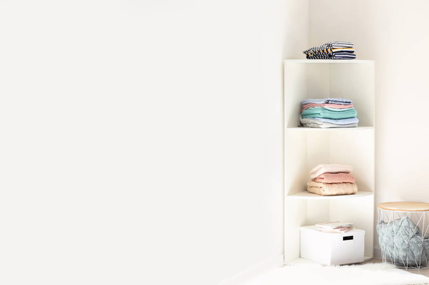 Rack with stacks of clean clothes near white wall - Zdjęcie, obraz