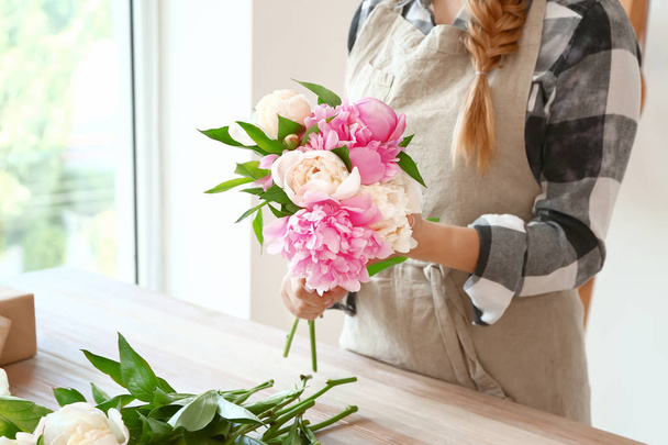 Female florist with beautiful bouquet of peonies in shop - Фото, изображение