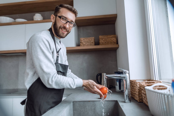 young man washing tomatoes under the tap in the kitchen - Photo, Image
