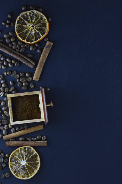 Fresh natural coffee beans scattered on a dark blue background with cinnamon sticks, sliced orange slices - Фото, изображение