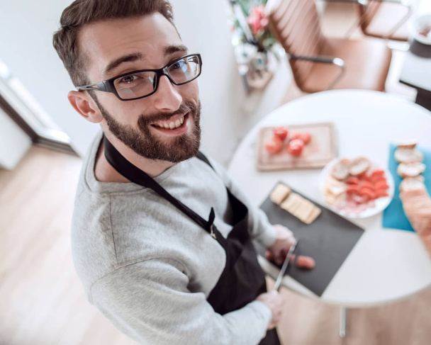 close up. smiling young man slicing salami - Zdjęcie, obraz