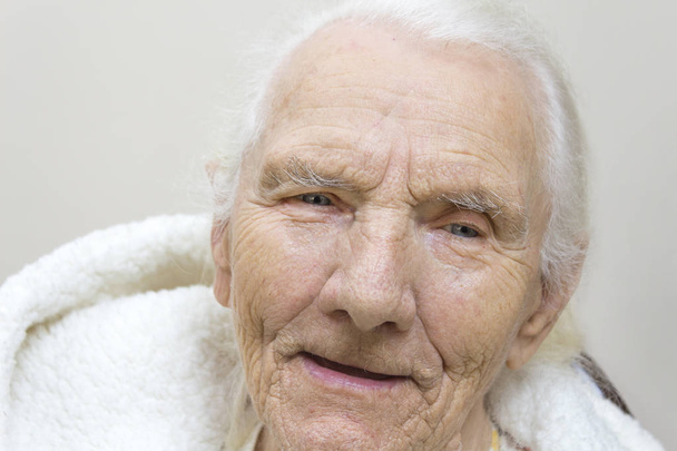 Muotokuva hymyilevä harmaa tukka hyvin vanha nainen kylpytakissa hupparilla.Kasvot hyvin vanha harmaa nainen ilman hampaita
. - Valokuva, kuva