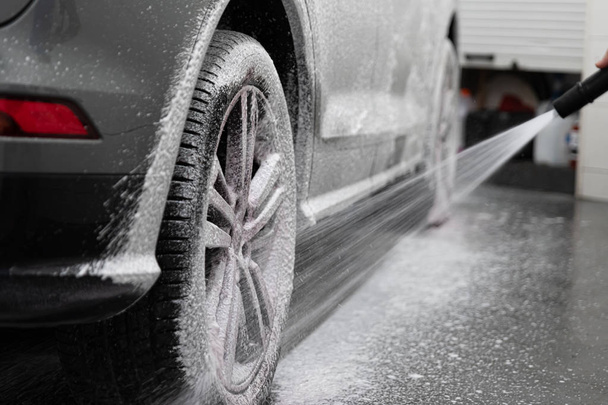 Εργαζόμενος πλυσίματος αυτοκινήτων ψεκασμός τροχού αυτοκινήτου και ελαστικών με λευκό ενεργό αφρό καθαρισμού - Φωτογραφία, εικόνα