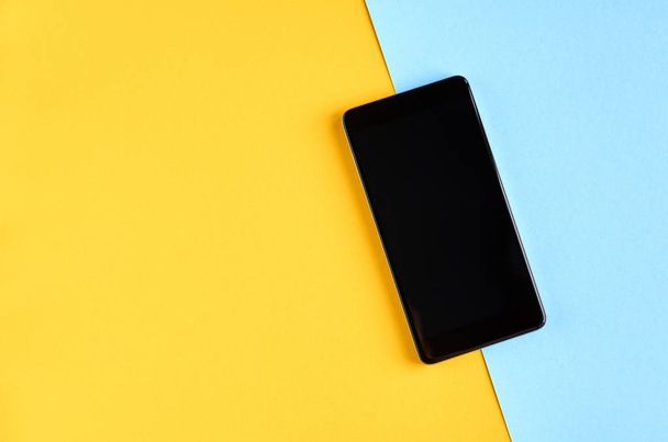 Black cellphone on yellow and blue background composition, mobile phone. - Foto, Bild