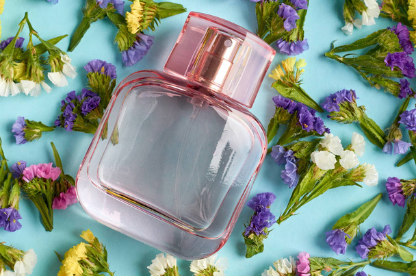 Perfume bottle with colored flowers on blue background composition. - Foto, imagen