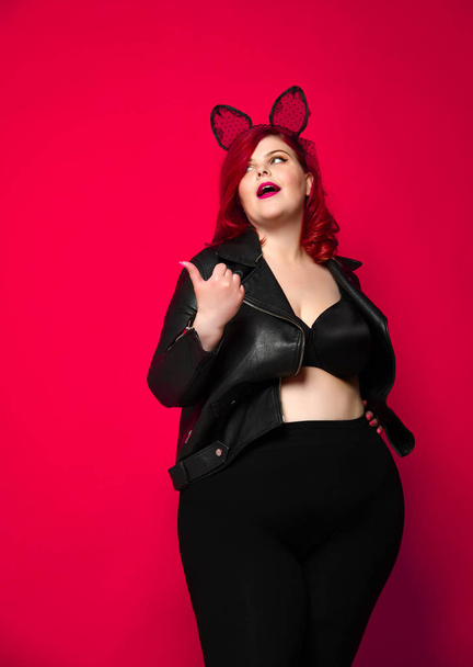 Cute sexy plus size brunette with black bunny ears in leather jacket and underwear posing on red background - 写真・画像
