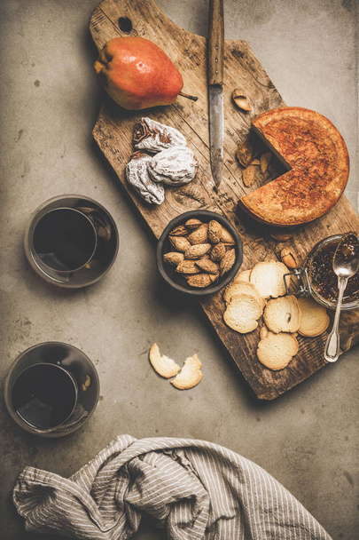 Wine and snack set. Flat-lay of two glasses of red wine, vintage corkscrews, cheese and appetizers on wooden board over grey concrete background, top view. Party food concept - Foto, Imagem