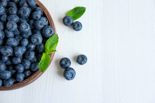 Closeup of blueberry berries with mint leaves in a clay plate on a light wooden background. Photo of blueberry for designers on the banner. Useful berries for sight - Photo, Image