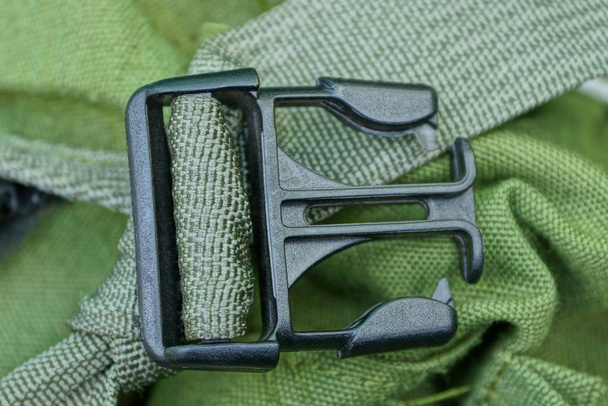 un gancho a presión de plástico abierto negro en un arnés verde en una tela de mochila
 - Foto, imagen