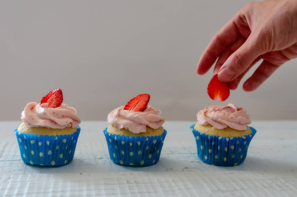 womans hand decorating muffins with strawberries white - Φωτογραφία, εικόνα