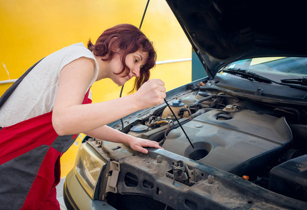 Female mechanic in red work wear checking car oil. Gender equality, diversity - Photo, Image