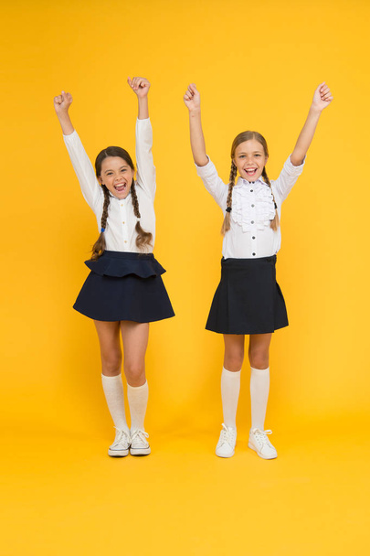 Celebrating back to school. Happy girls celebrating achievement in study on yellow background. Small cute schoolchildren celebrating and making winner gestures. Keep celebrating school holidays - Foto, afbeelding