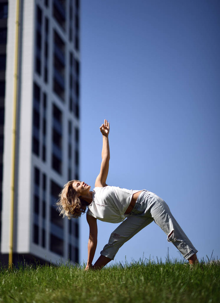 Young woman doing yoga stretching exercises in urban modern city park - Photo, Image