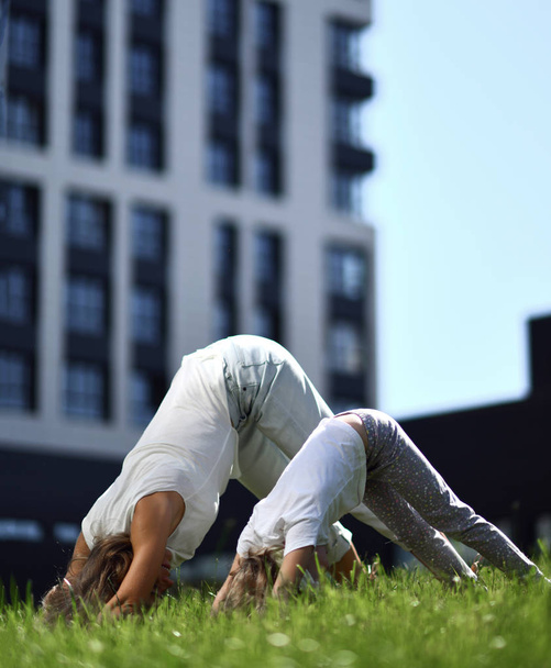 Mother and daughter working out practicing yoga outside on a grass together urban city  park  - 写真・画像