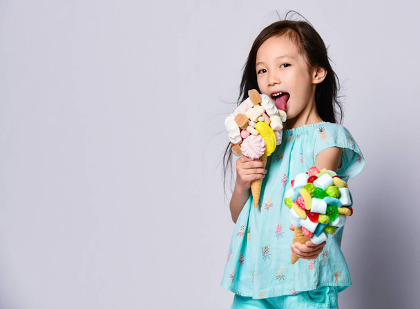 Happy asian baby girl kid eats licks a big ice-cream in waffles cones with tasty toppings and offers another one us - Фото, изображение