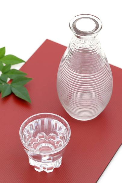 sake japonés en taza de vidrio transparente y frasco sobre fondo rojo
 - Foto, imagen