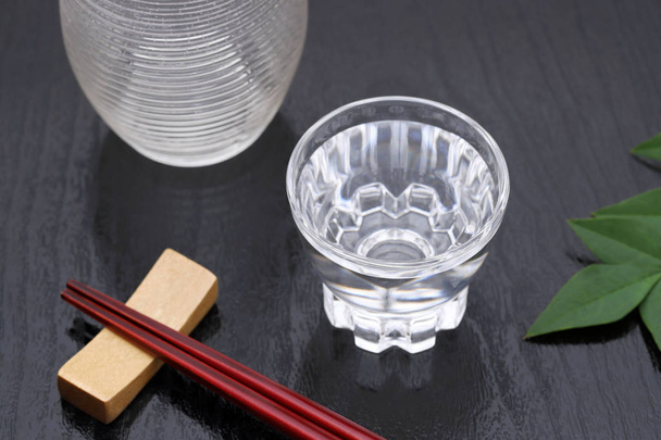 Saquê japonês em copo de vidro transparente e frasco no fundo preto
 - Foto, Imagem