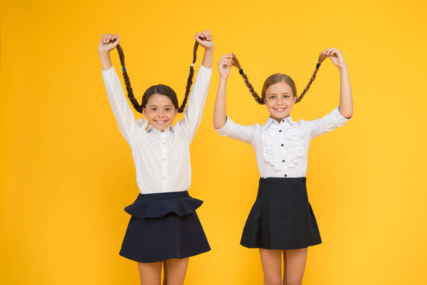 Long hair growth stimulant. Cute small children holding long hair braids on yellow background. Adorable little girl being proud of long hair. Wearing long hair in plaits for school - 写真・画像