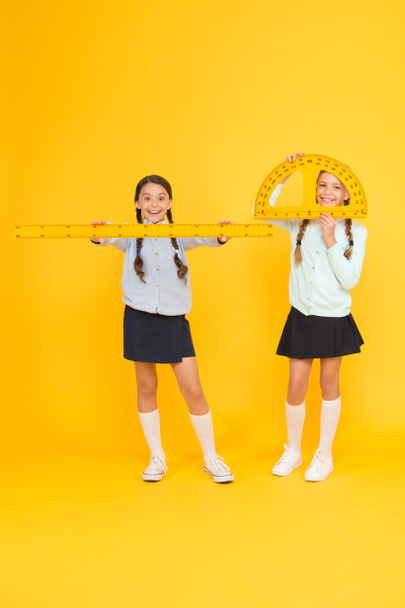 Learning school geometry. School children with measuring instruments on yellow background. Cute pupils holding protractor and ruler for school lesson. Small girls are back to school - Φωτογραφία, εικόνα