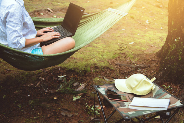 Kadınlar doğal olarak hamakta otururken ve bir dizüstü bilgisayar kullanarak doğal bir parkta çalışırlar.. - Fotoğraf, Görsel