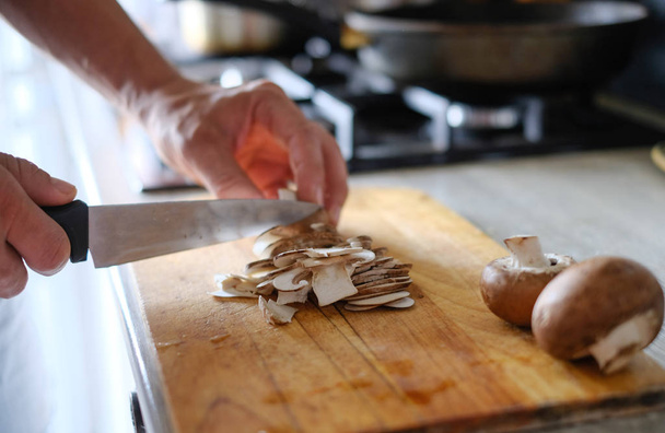 Homme mains coupées champignons sur la planche en bois dans la cuisine de la maison
 - Photo, image