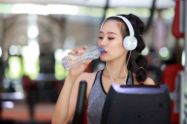 Женщина в наушниках пьет воду после кардиотренировок в фитнес-зале
. - Фото, изображение