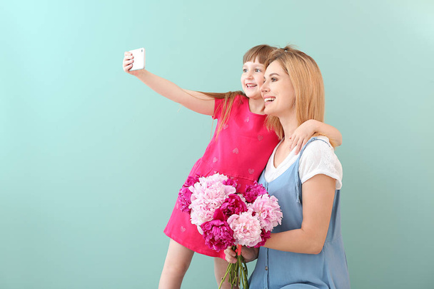 Little girl and her mother taking selfie with flowers on color background - Photo, Image