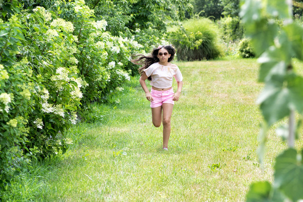 Sporty young girl running in a garden on the lawn - Fotoğraf, Görsel