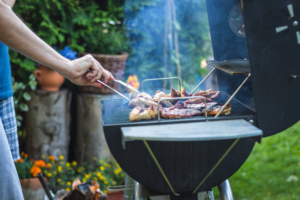 Κρέας μπάρμπεκιου στη σχάρα κατά τη διάρκεια του πάρτι στον κήπο. Άνθρωπος μαγείρεμα μαριναρισμένο φαγητό το καλοκαίρι BBQ σε εξωτερικούς χώρους - Φωτογραφία, εικόνα
