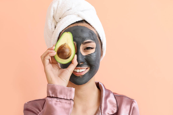 Beautiful Asian woman with facial mask and avocado on color background - Foto, Imagem