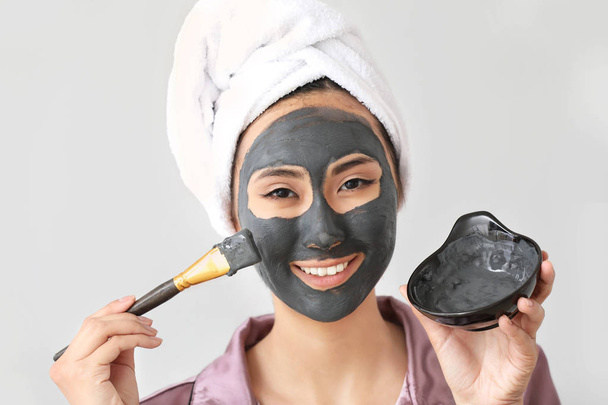schöne asiatische Frau Anwendung Gesichtsmaske vor hellem Hintergrund - Foto, Bild