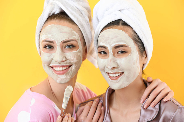 Mooie jonge vrouwen met gezichtsmaskers op kleur achtergrond - Foto, afbeelding