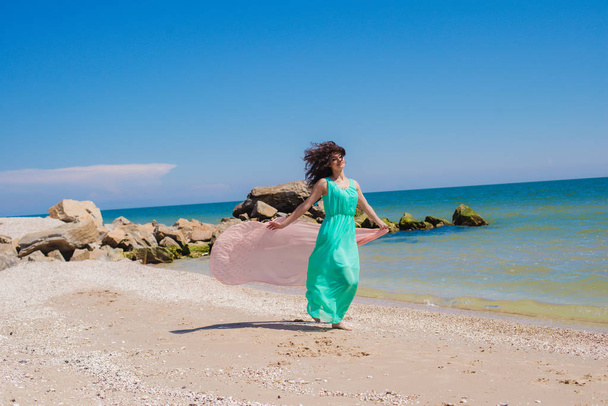 Young girl on the beach in summer in a beautiful dress with a flying scarf  - Photo, image