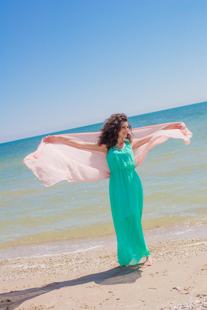 Young girl on the beach in summer in a beautiful dress with a flying scarf  - Φωτογραφία, εικόνα