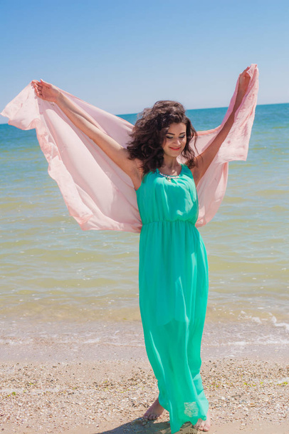 Young girl on the beach in summer in a beautiful dress with a flying scarf  - Foto, Bild