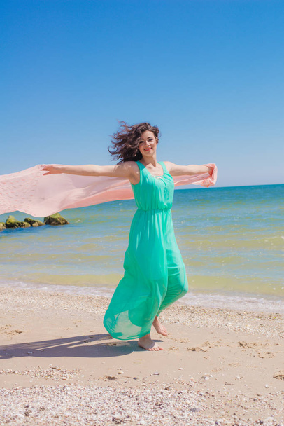 Young girl on the beach in summer in a beautiful dress with a flying scarf  - Foto, afbeelding