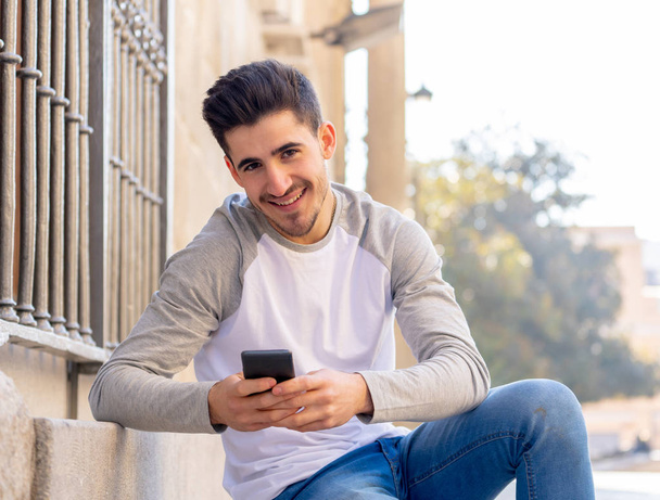 Young attractive man in his twenties happy talking and chatting with friend on social media on smart phone on holidays in europe. In communication, technology internet and lifestyle concept. - Photo, Image